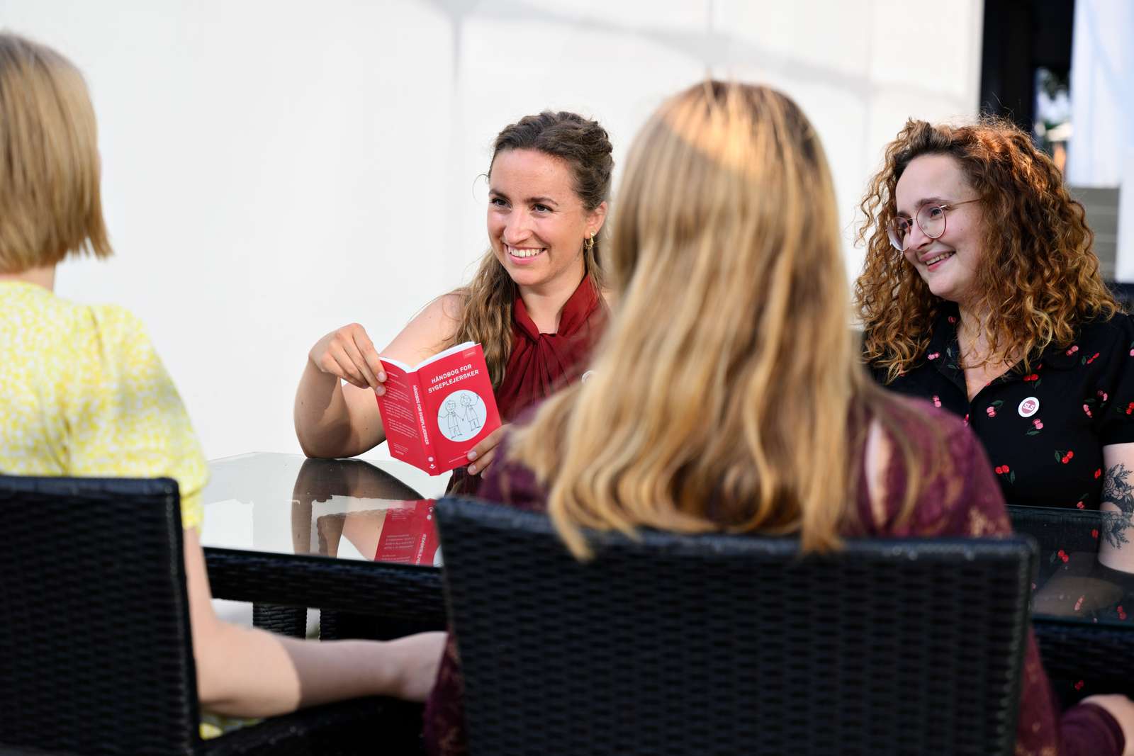 SLS-aktive griner sammen ved et bord udendørs med håndbog for sygeplejersker